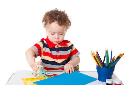 Young boy at desk cutting colored paper with scissors